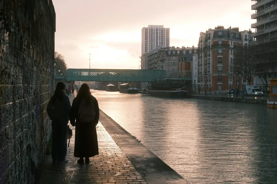 Twee personen lopen langs een kade aan het water bij zonsondergang